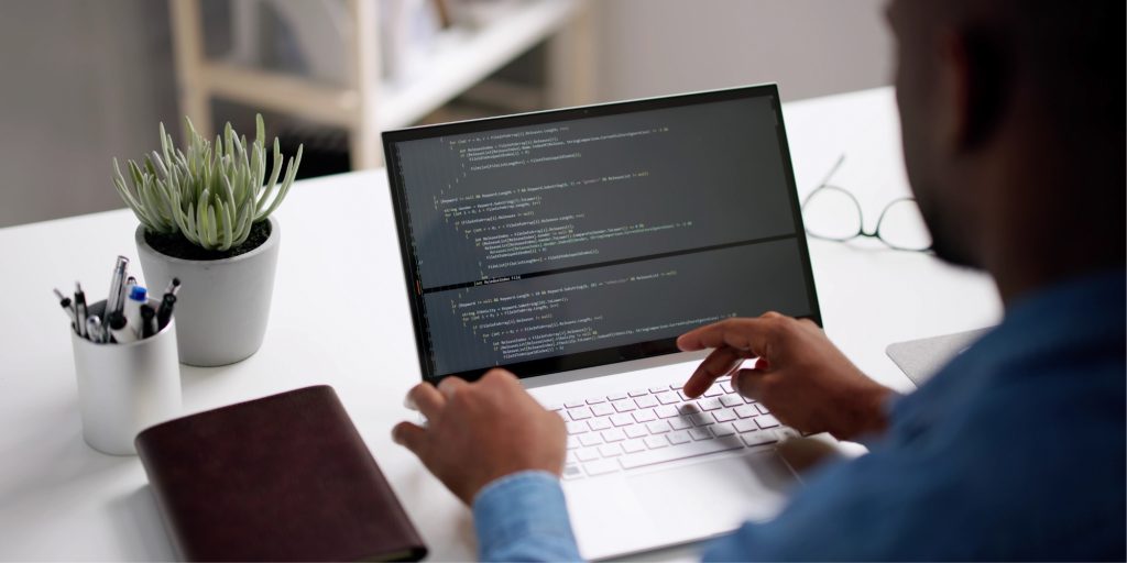 Un homme de dos assis à un bureau, en train de coder un site